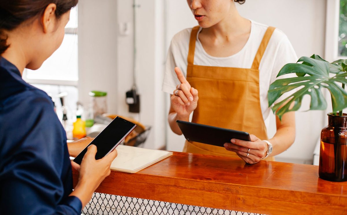 お店のカウンターで、店員がタブレットを、お客様がスマートフォンを手に話している様子
